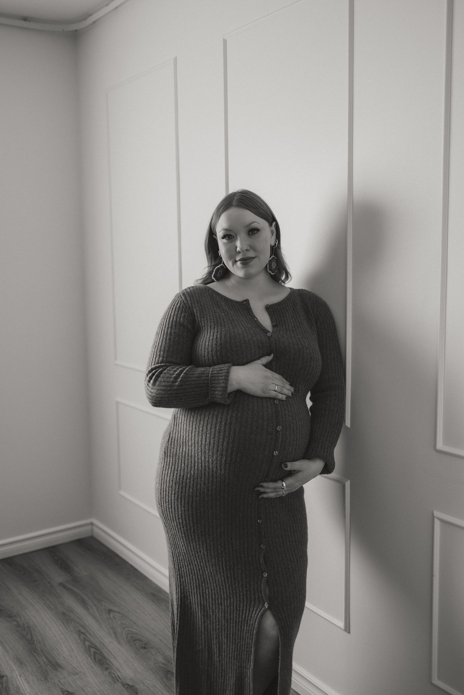 Black-and-white maternity portrait of an expecting mother in a fitted knit dress, cradling her bump.
