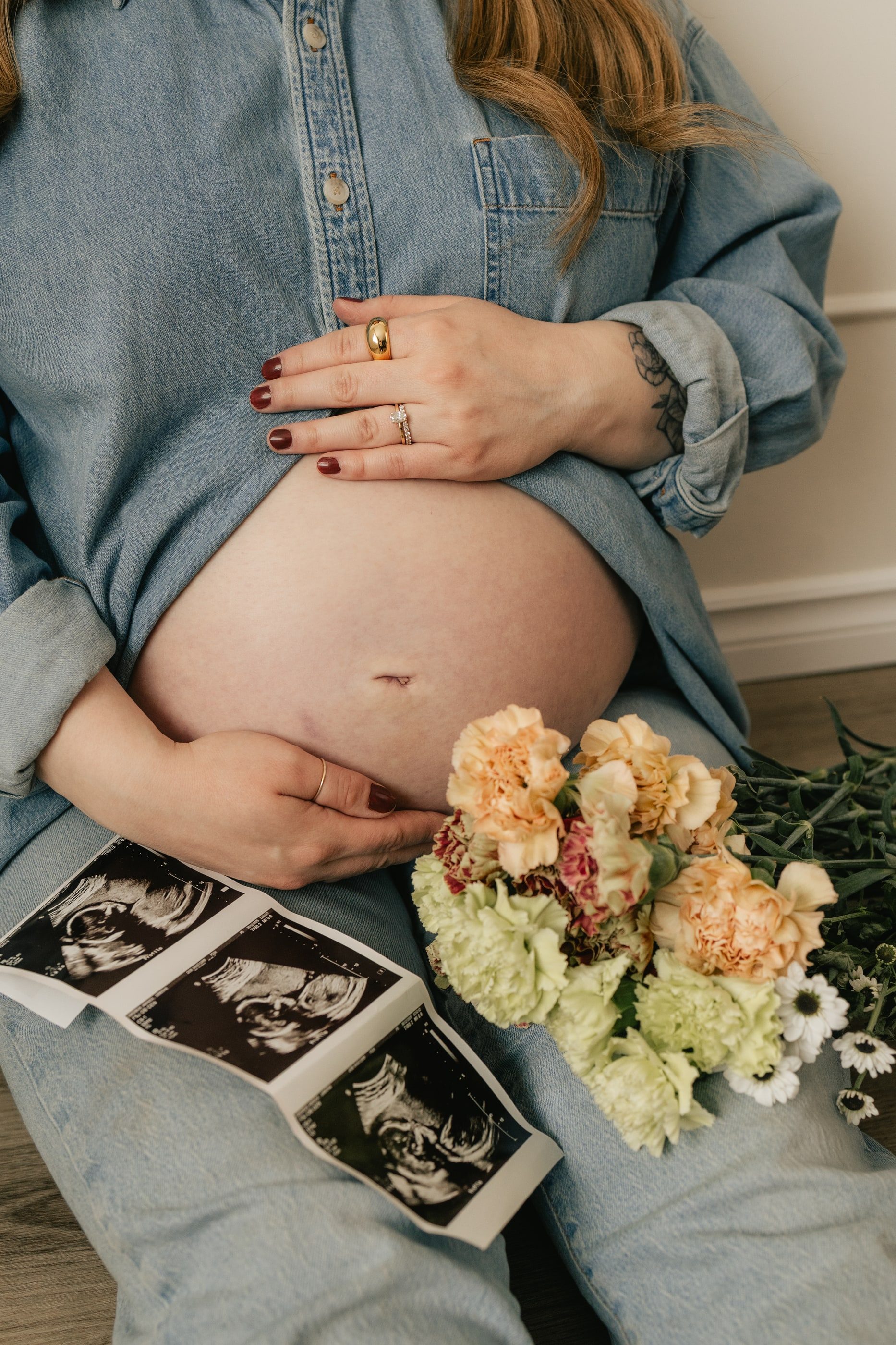 Close-up of an expecting mother's bump, with ultrasound photos and a bouquet of peach flowers in her lap.