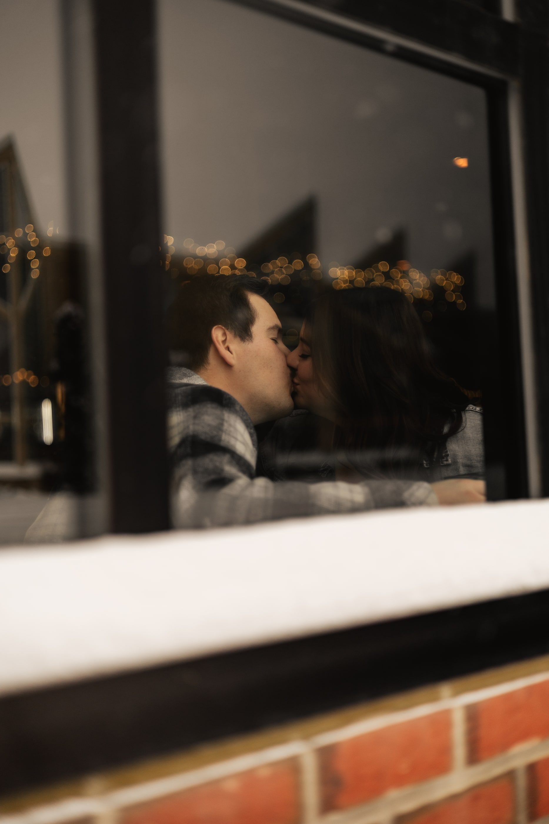 A couple kissing at a table inside a bar, seen through the window.