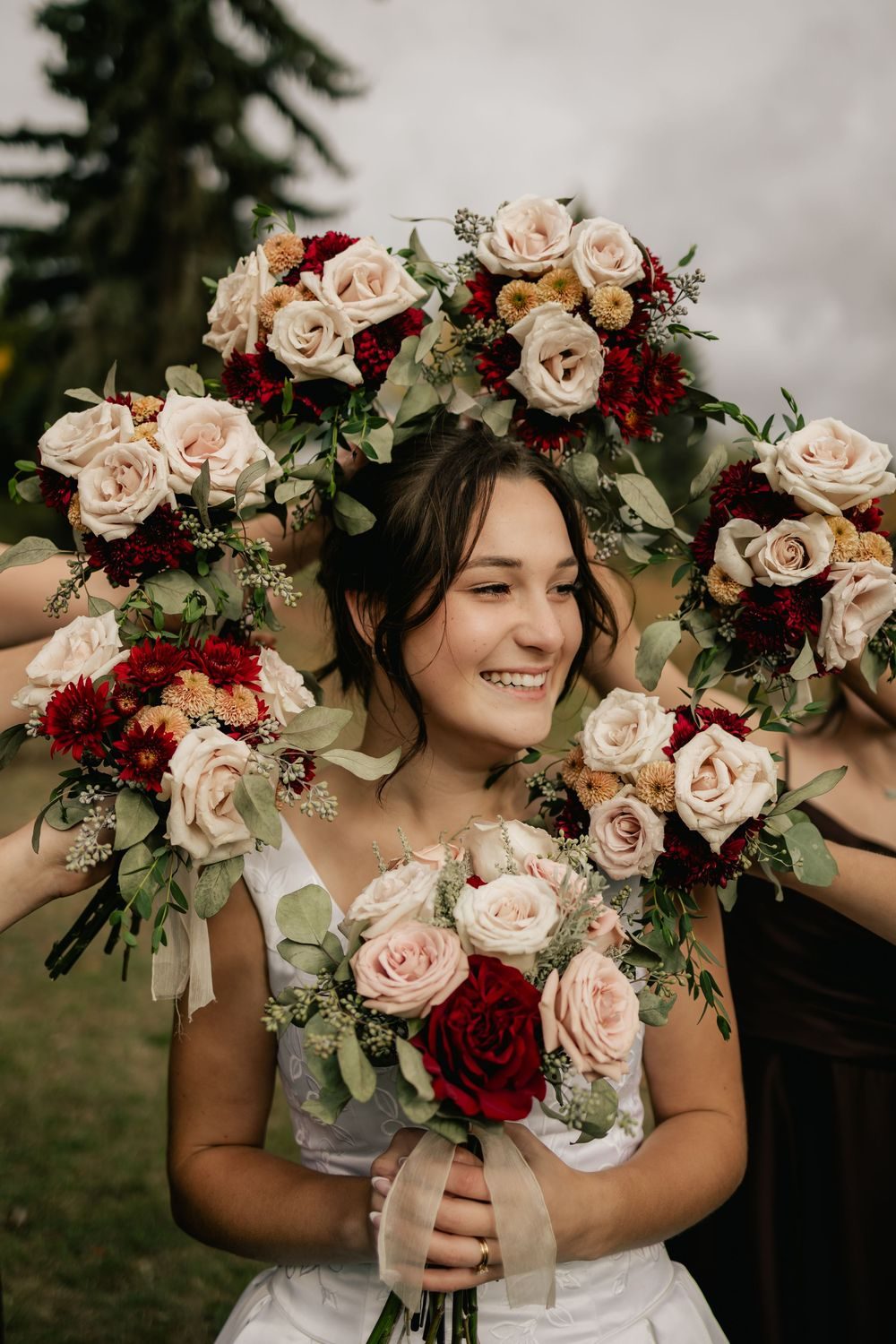A smiling bride framed by a circle of her bridesmaids' bouquets of blush and burgundy roses.