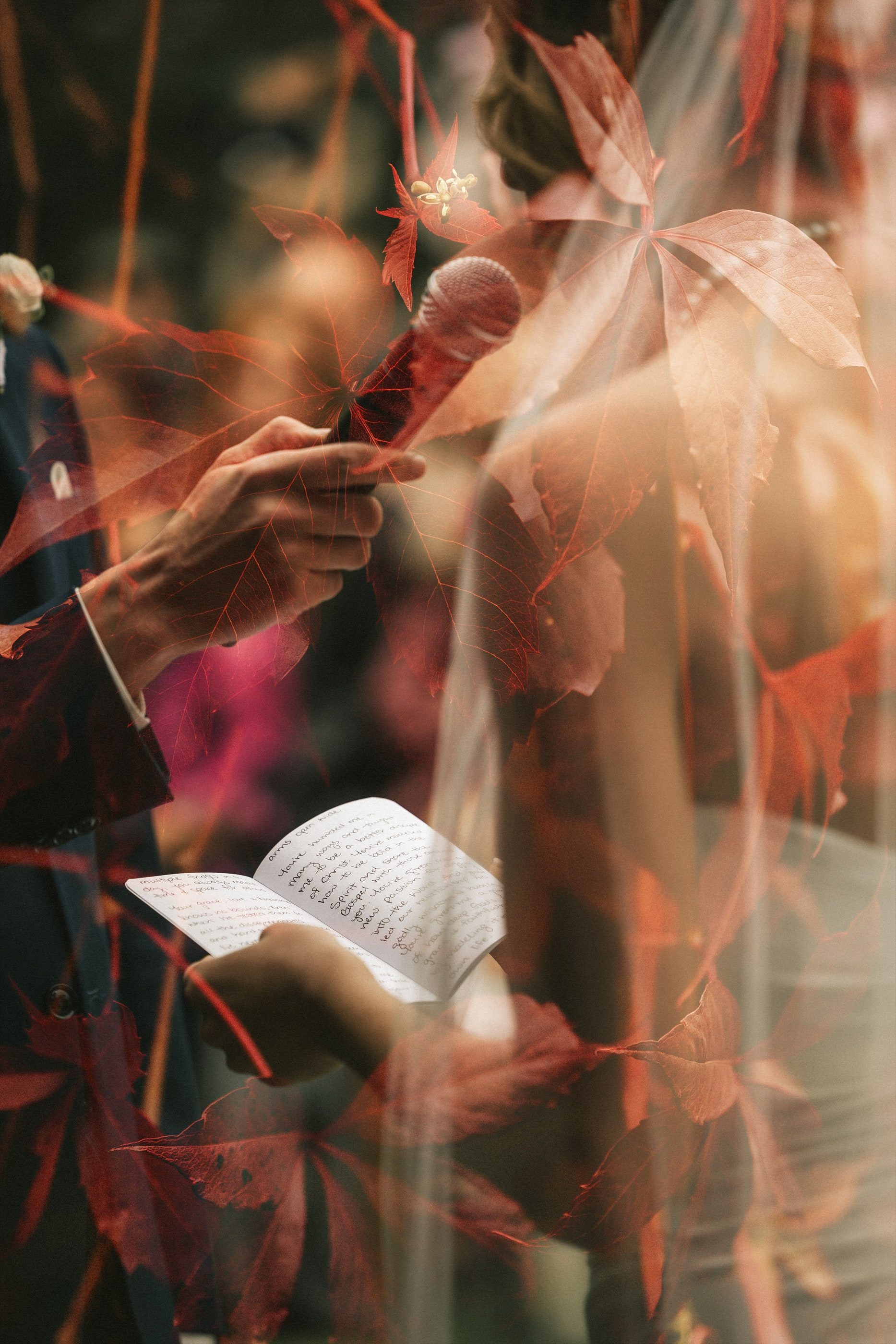A guest reads a speech into a microphone, seen through a veil of red autumn leaves.