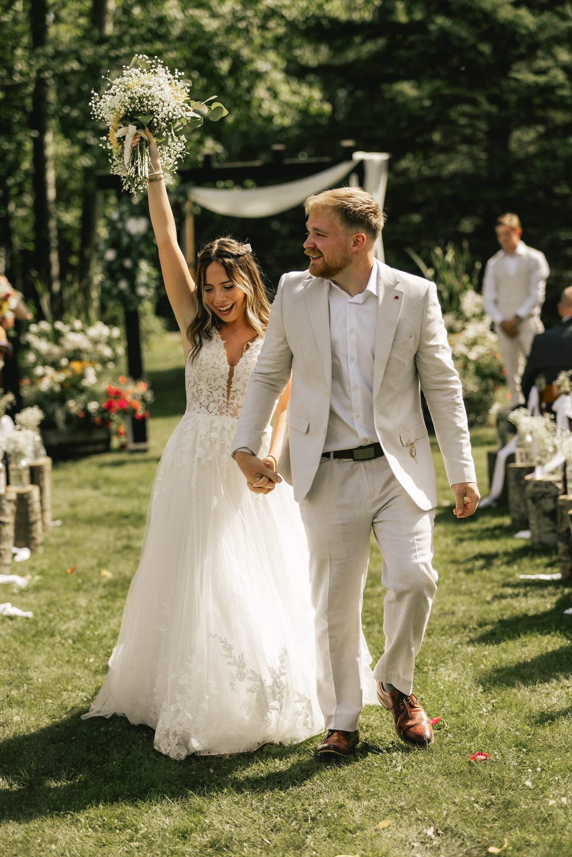 A bride raises her bouquet in celebration as she and her groom walk back up the aisle.