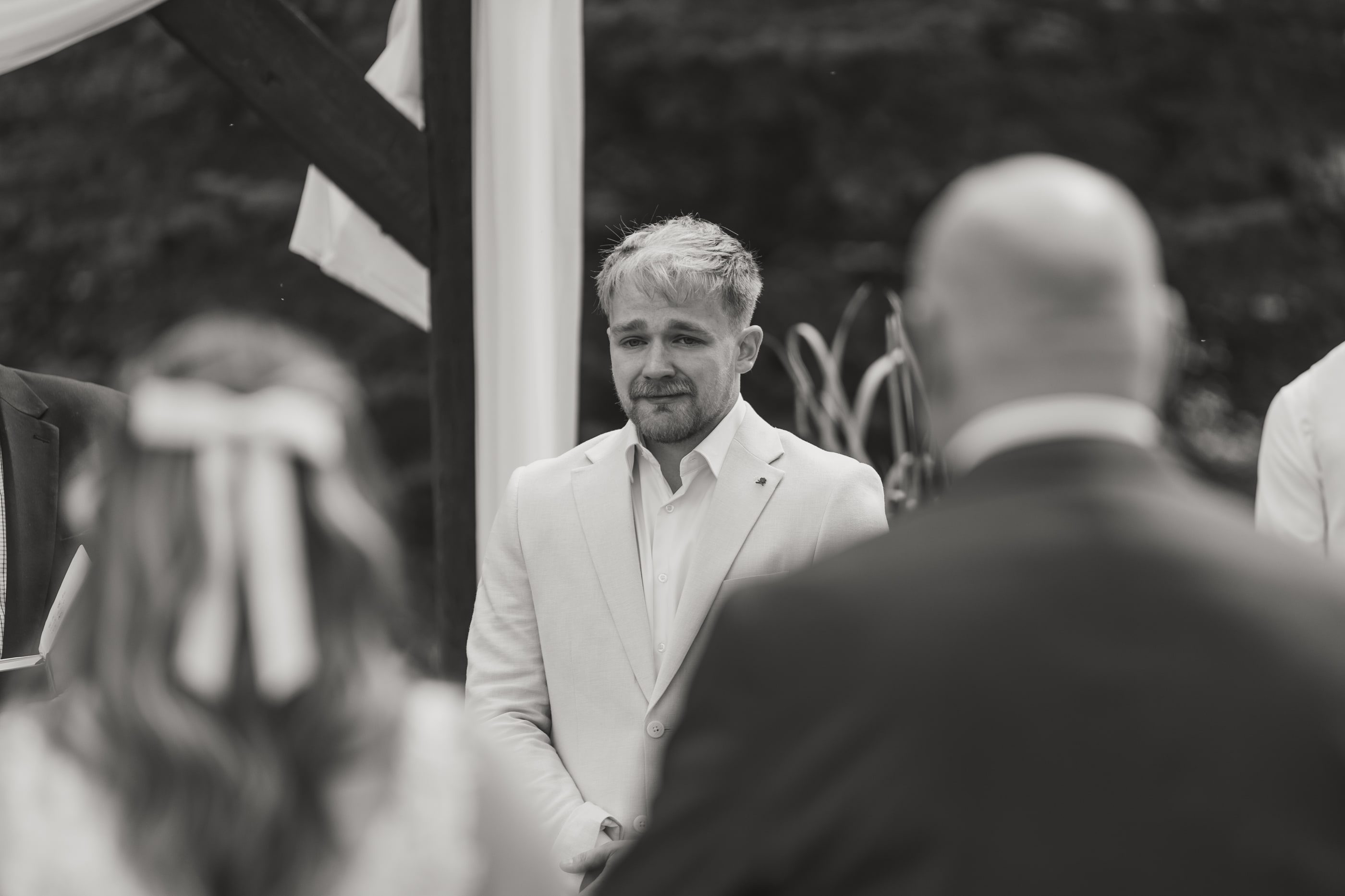 Black-and-white photo of a groom tearing up as his bride comes down the aisle.