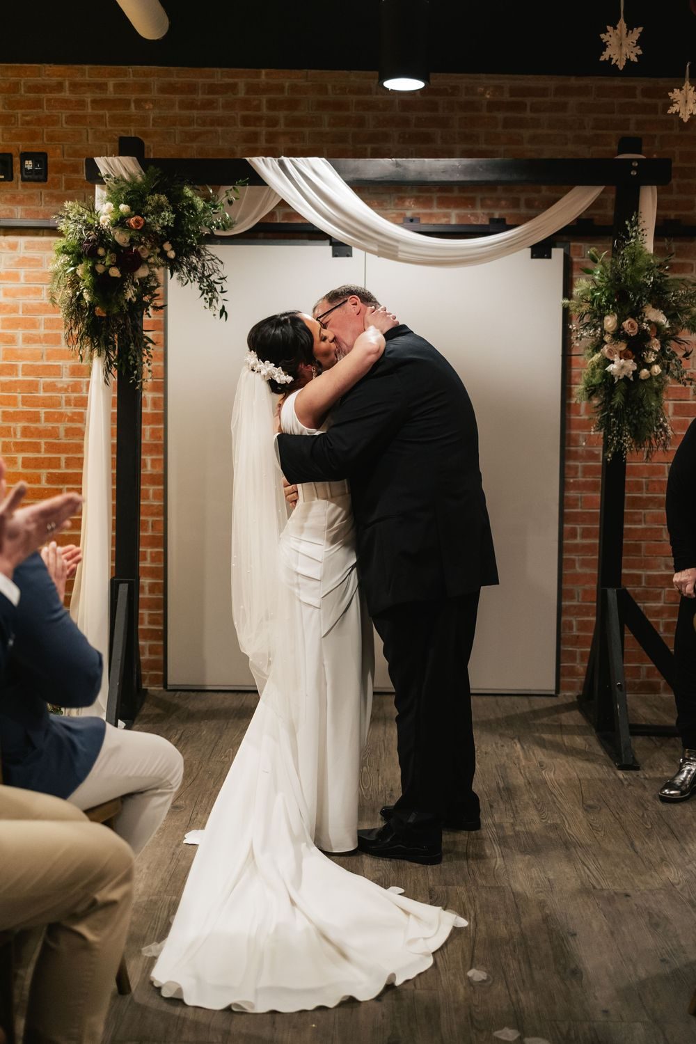 A bride and groom share their first kiss at the altar as guests look on.