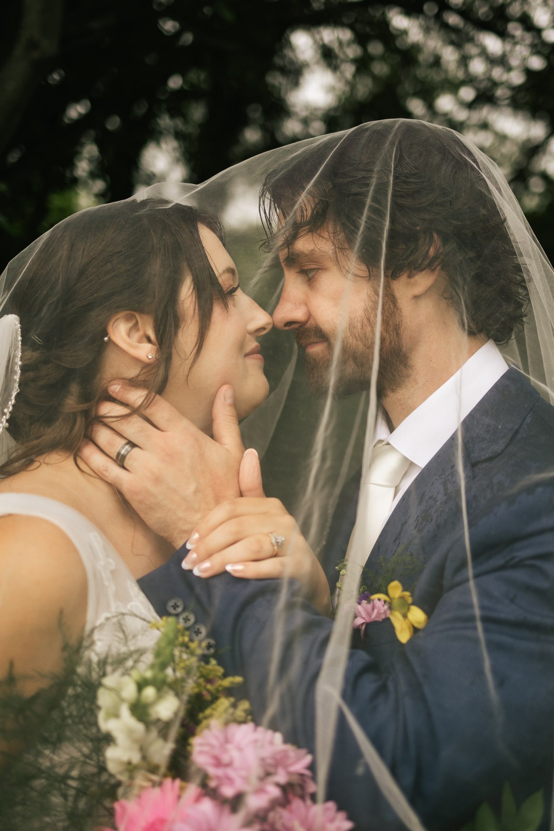 Beneath her veil, a bride holds her groom's face as they lean in close.