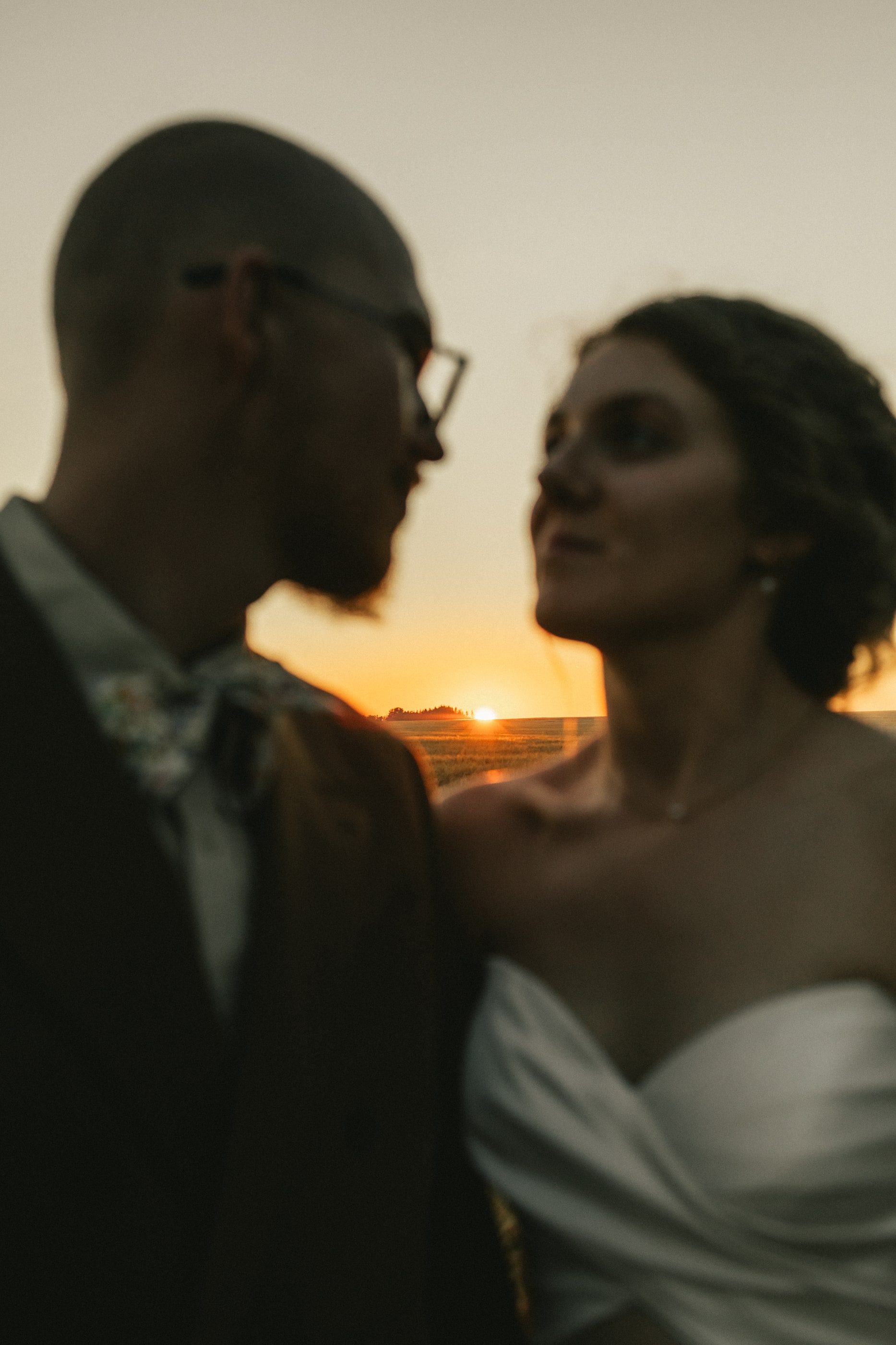 A bride and groom gaze at each other as the sun sets between them.