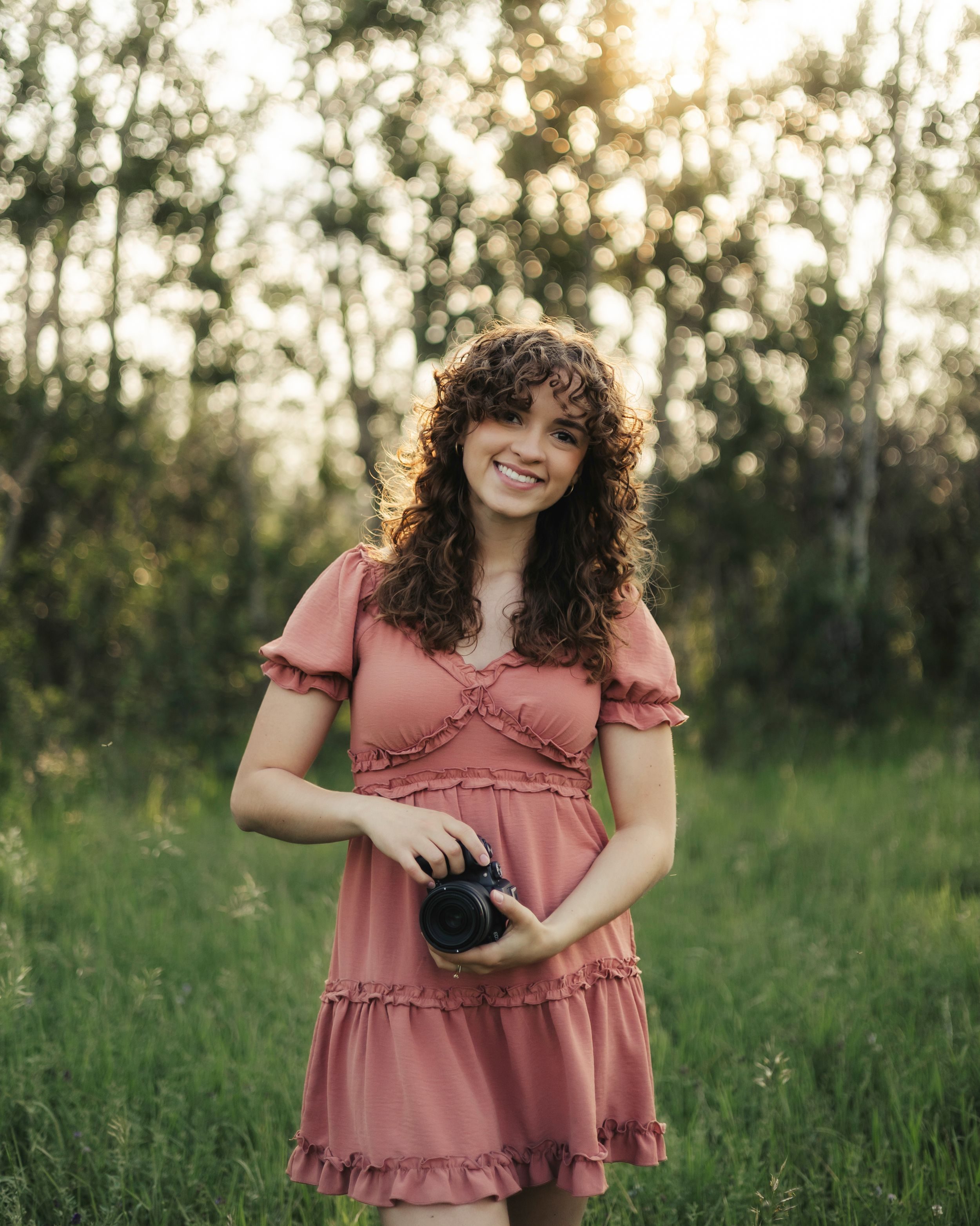 Emma Balderston smiling in a summer meadow, camera in hand.