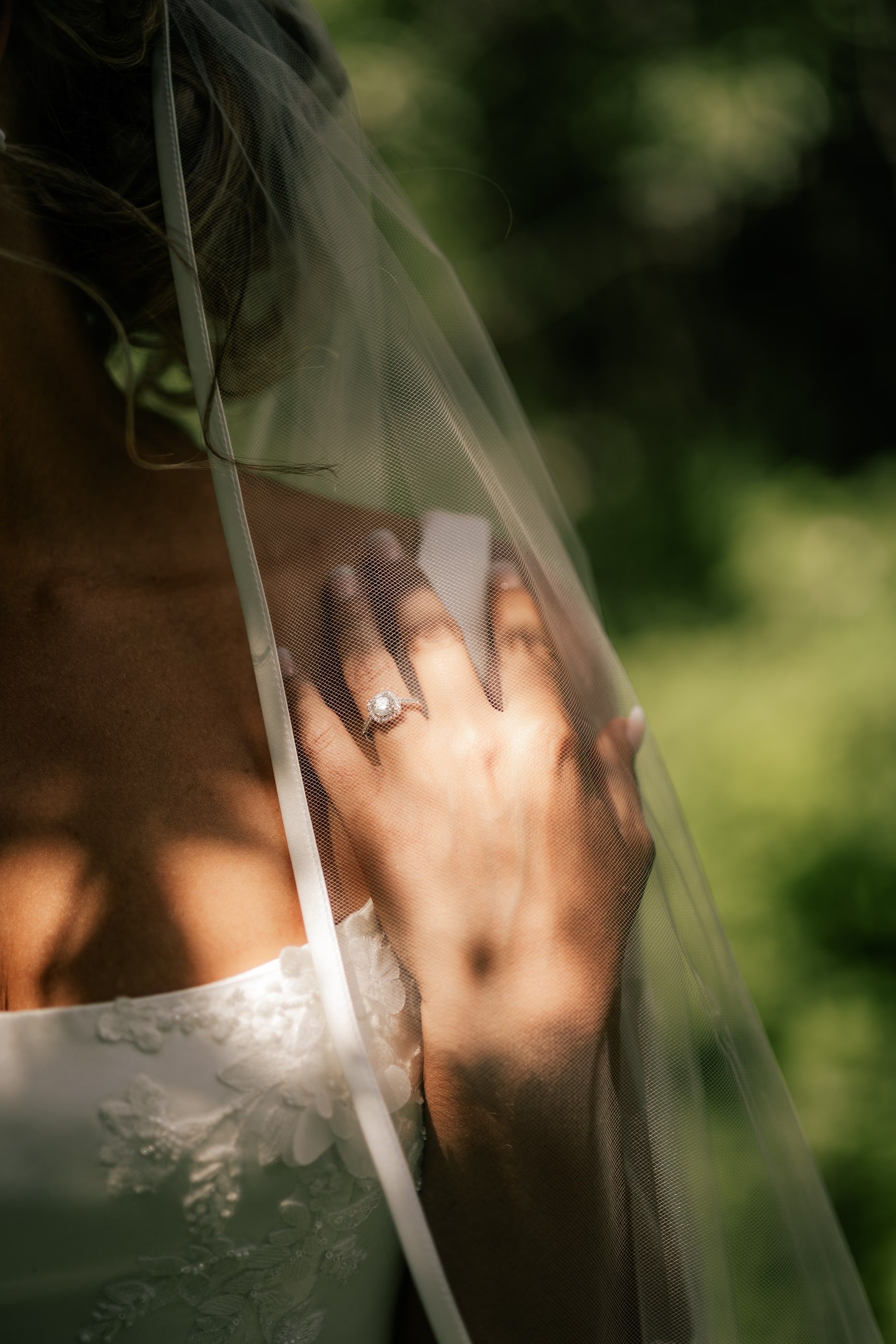 Close-up of a bride's hand and ring resting on her shoulder, her veil catching the light.