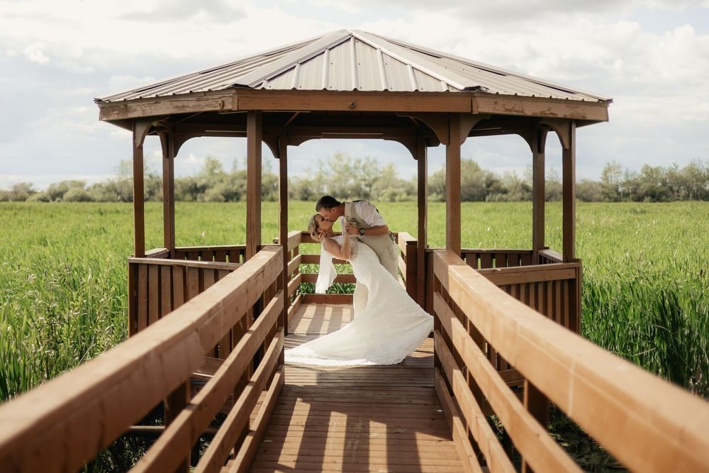 A bride and groom kiss in a wooden gazebo surrounded by green fields.