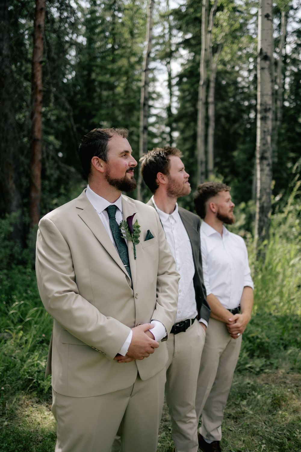 A groom in a linen suit shares a laugh with his groomsmen in the trees.