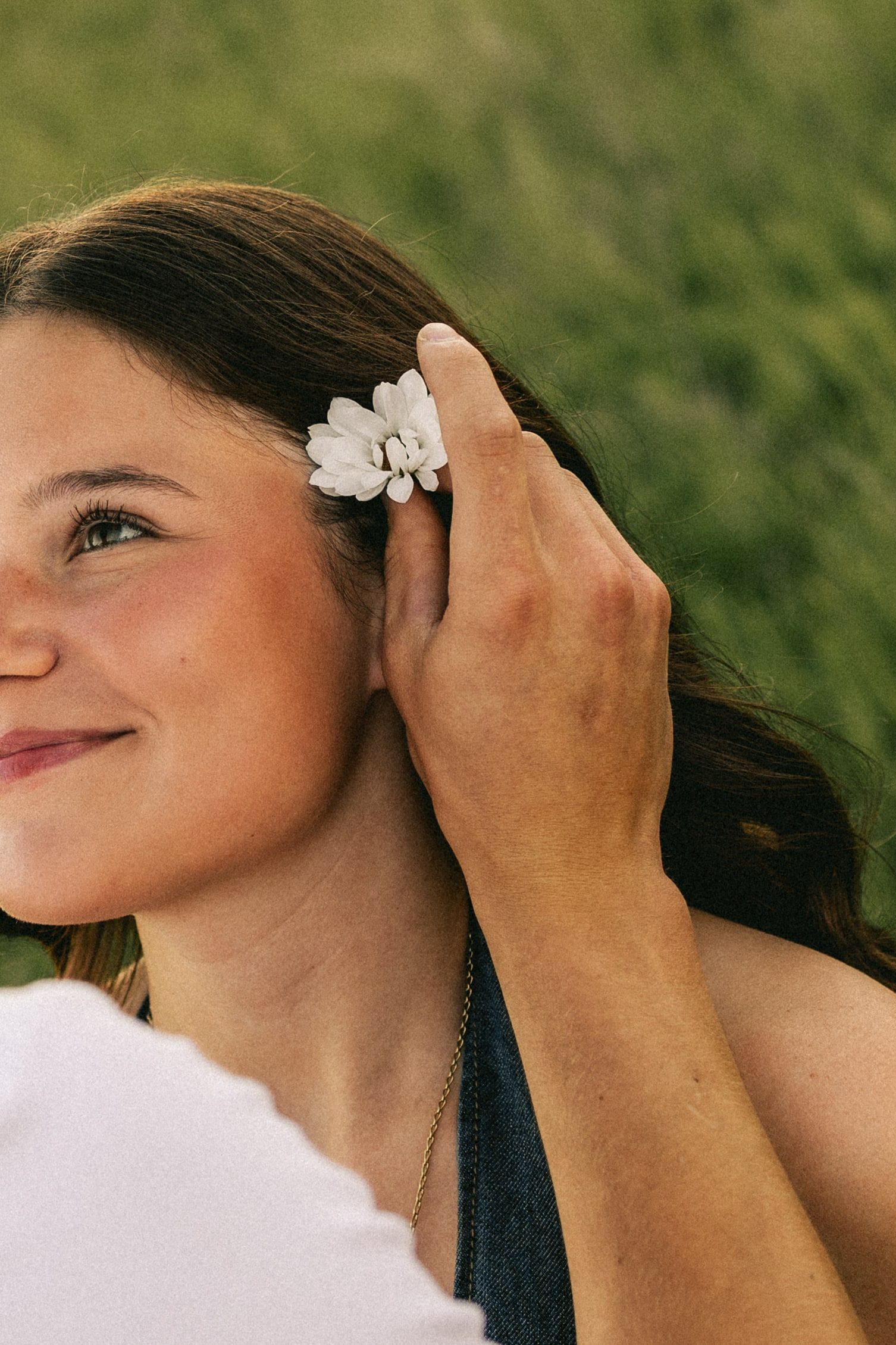Close-up of a smiling woman as her partner tucks a white flower behind her ear.