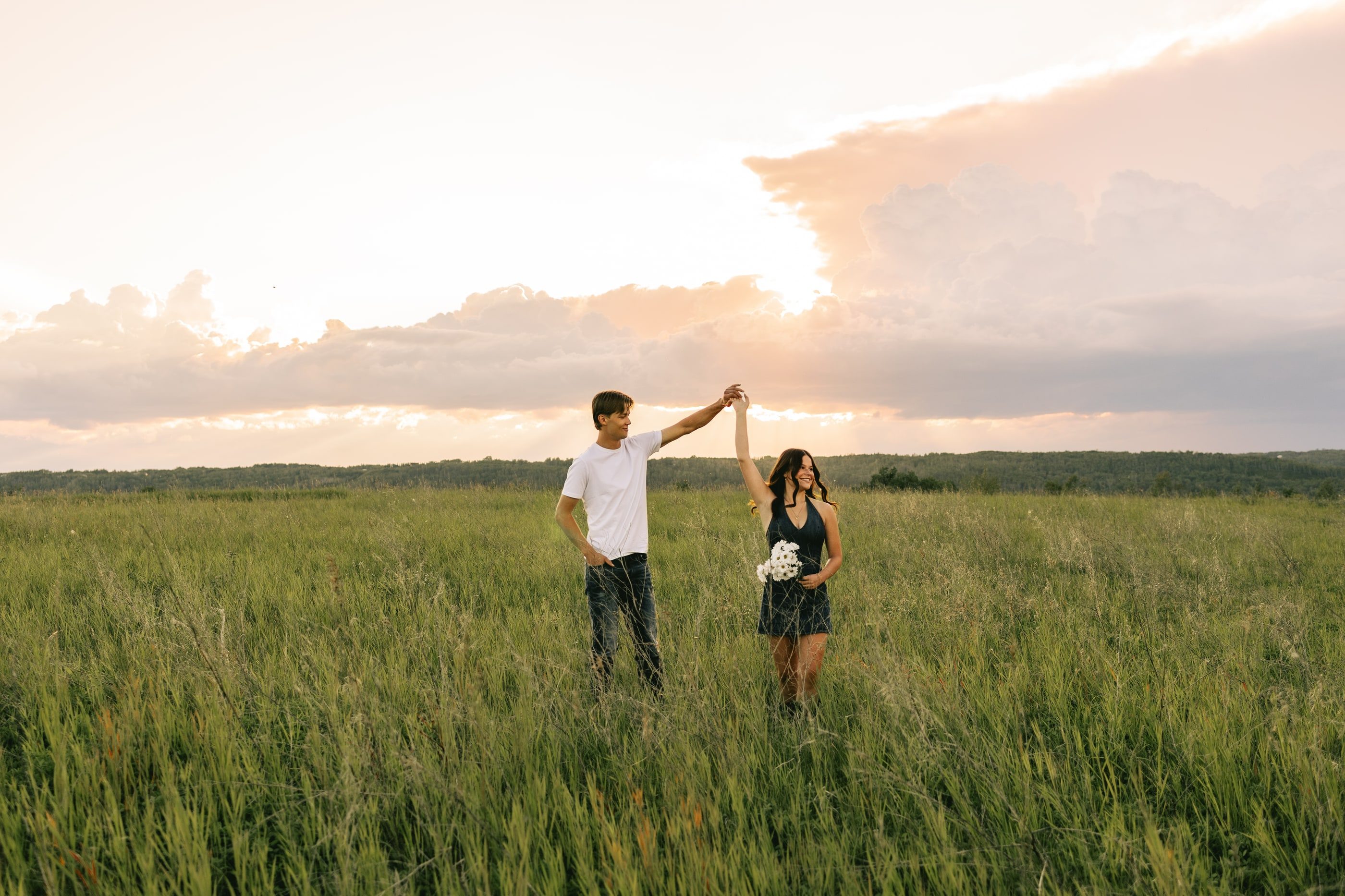 A man twirls his partner in a wide green field under a pink sunset sky.