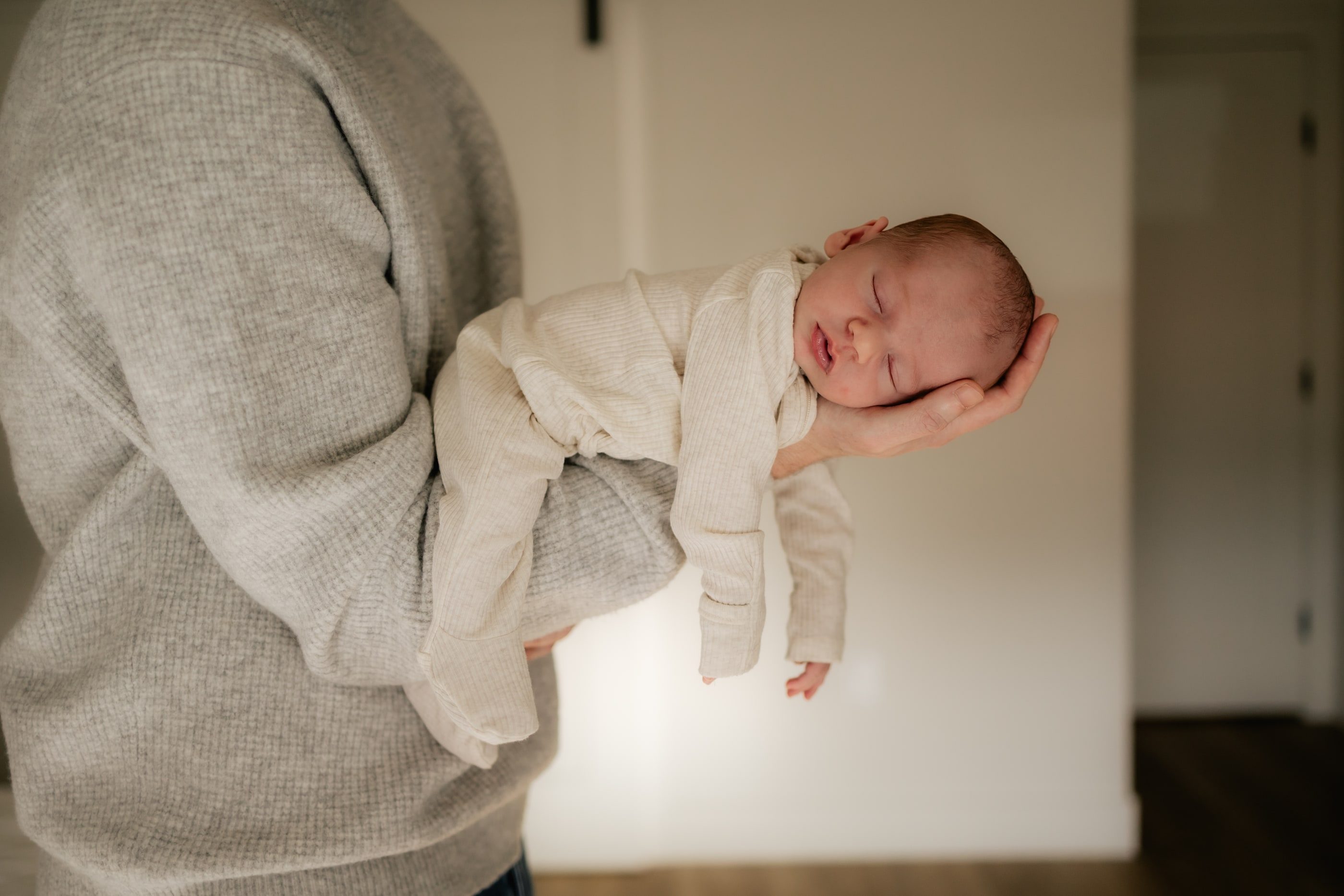 A father holds his sleeping newborn along his forearm, cradling the baby’s head in his hand.