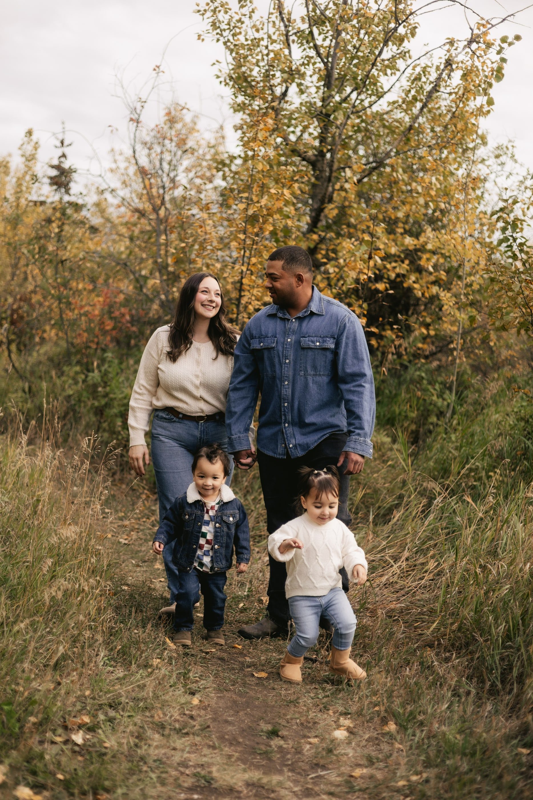 A family of four walks along a trail through autumn shrubs.