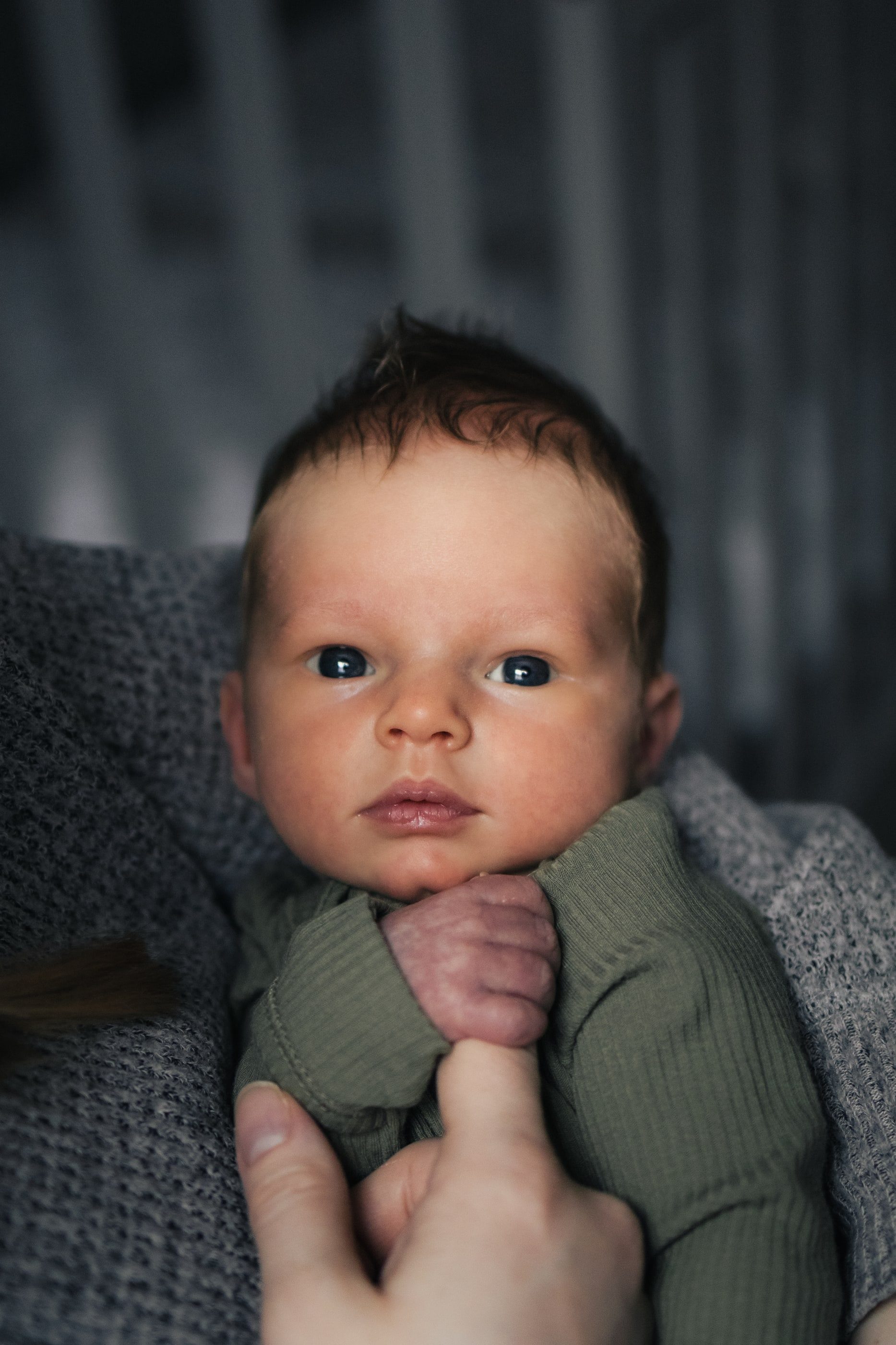 A newborn looks up wide-eyed, holding a parent's finger.