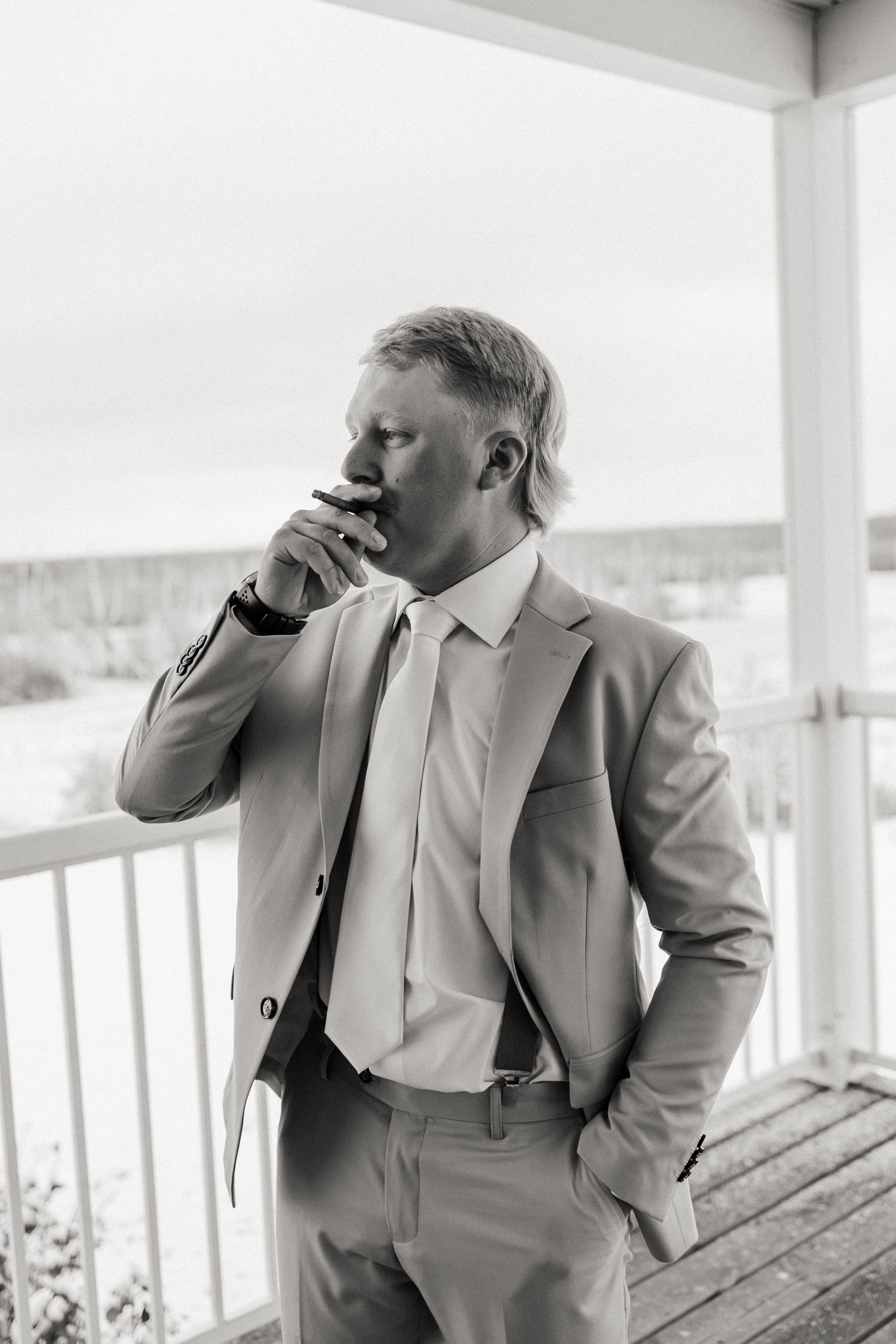 Black-and-white photo of a groom in a light suit wiping away a tear on a covered porch.
