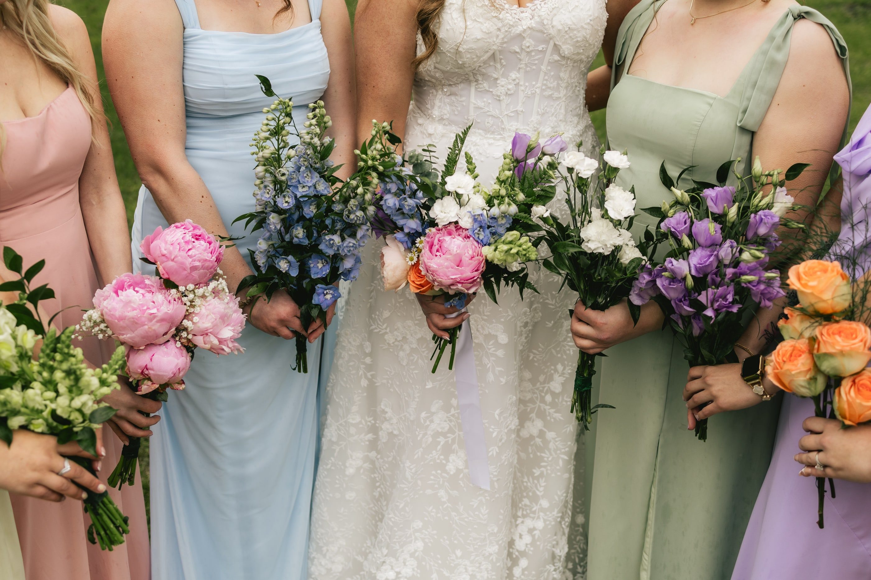Close-up of a bride and her bridesmaids in pastel dresses holding bouquets of peonies, roses and lisianthus.