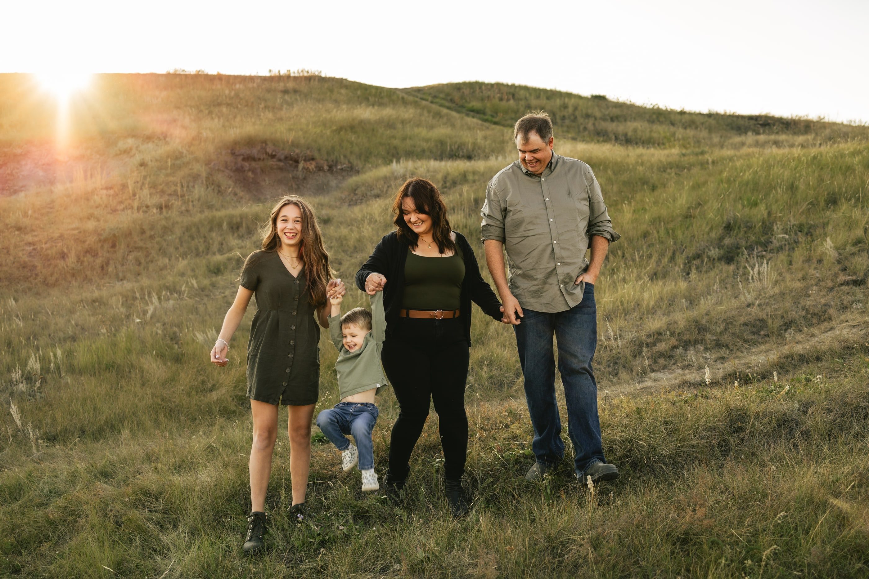 A family of four walks hand in hand down a grassy hill at sunset.