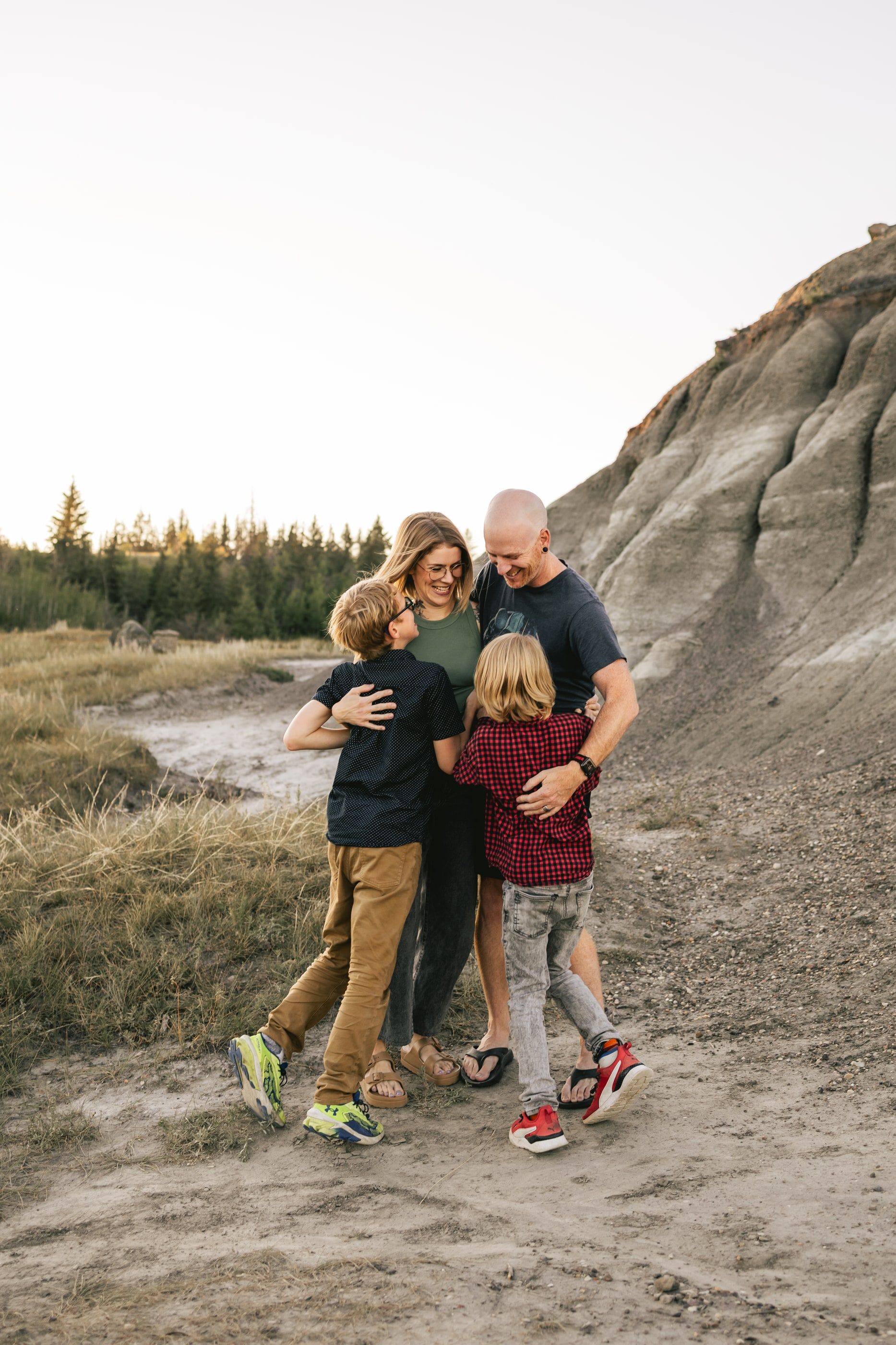 Parents hug their two young children on a sandy path below grey badlands hills.
