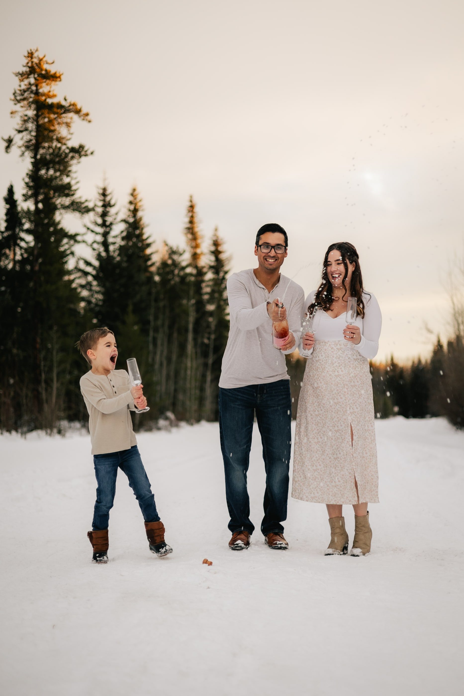 A family pops confetti poppers in the snow among evergreen trees.