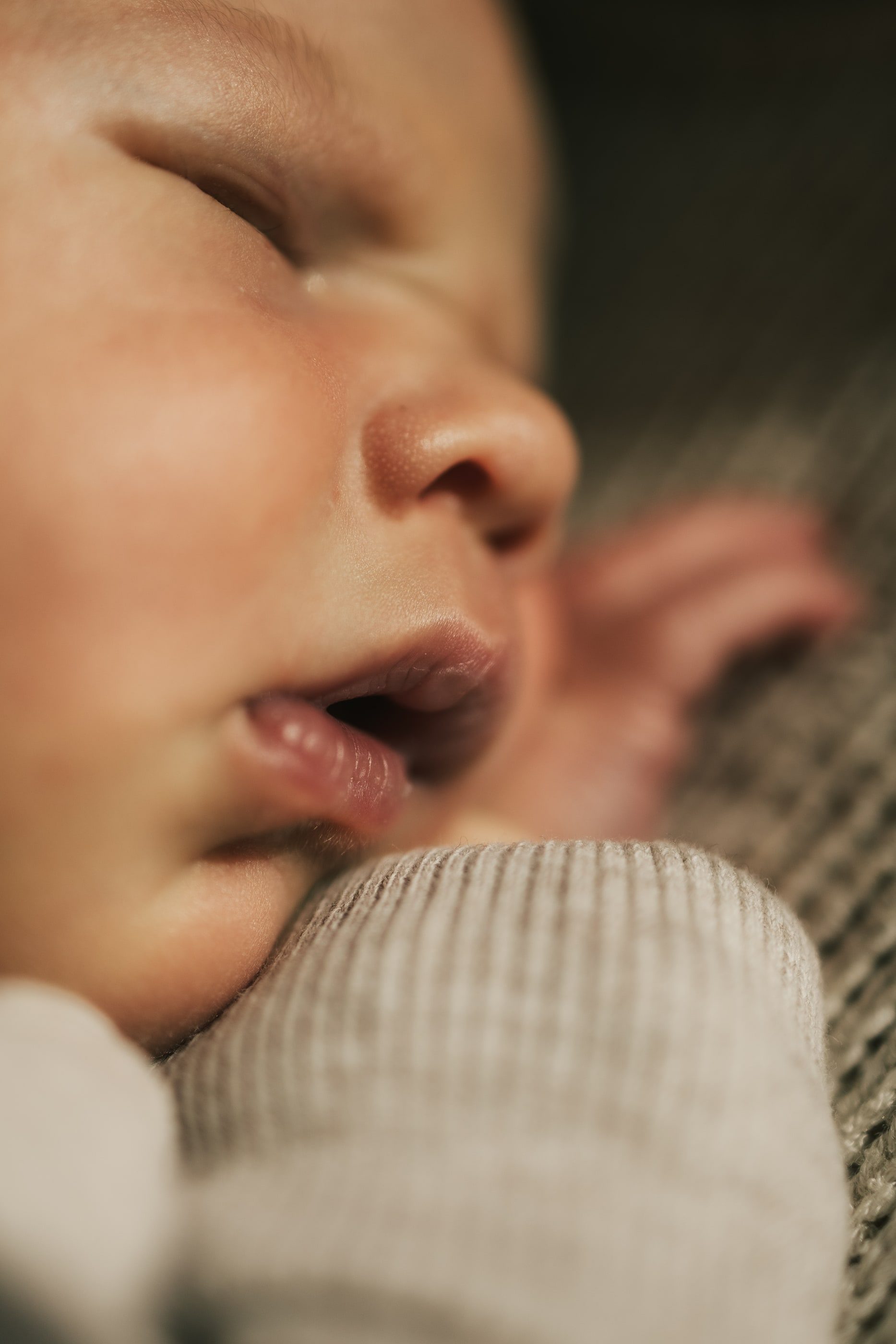 Close-up of a sleeping newborn's face resting against a knit sleeve.