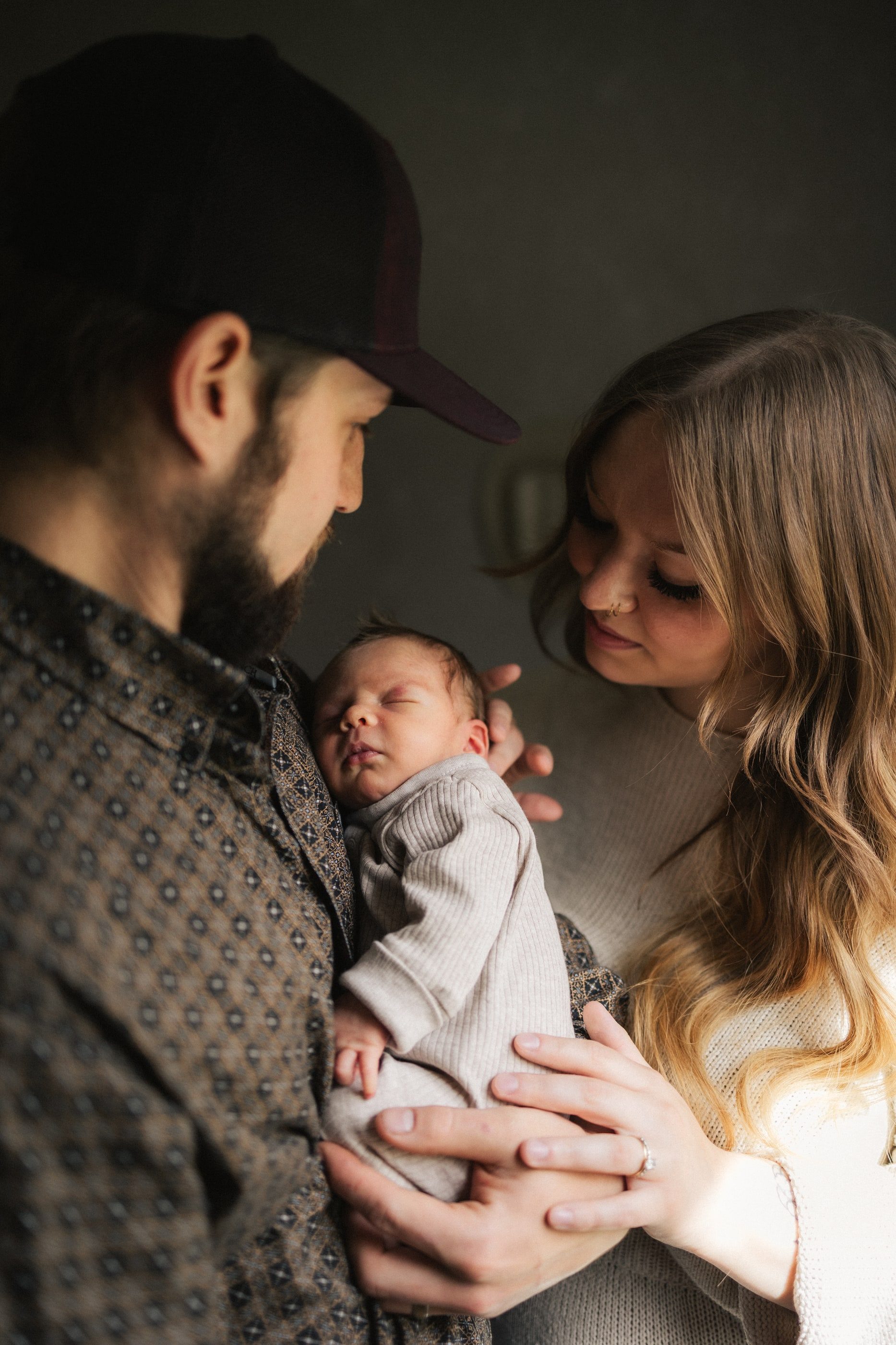 A father in a cap holds his newborn as the mother leans in close.