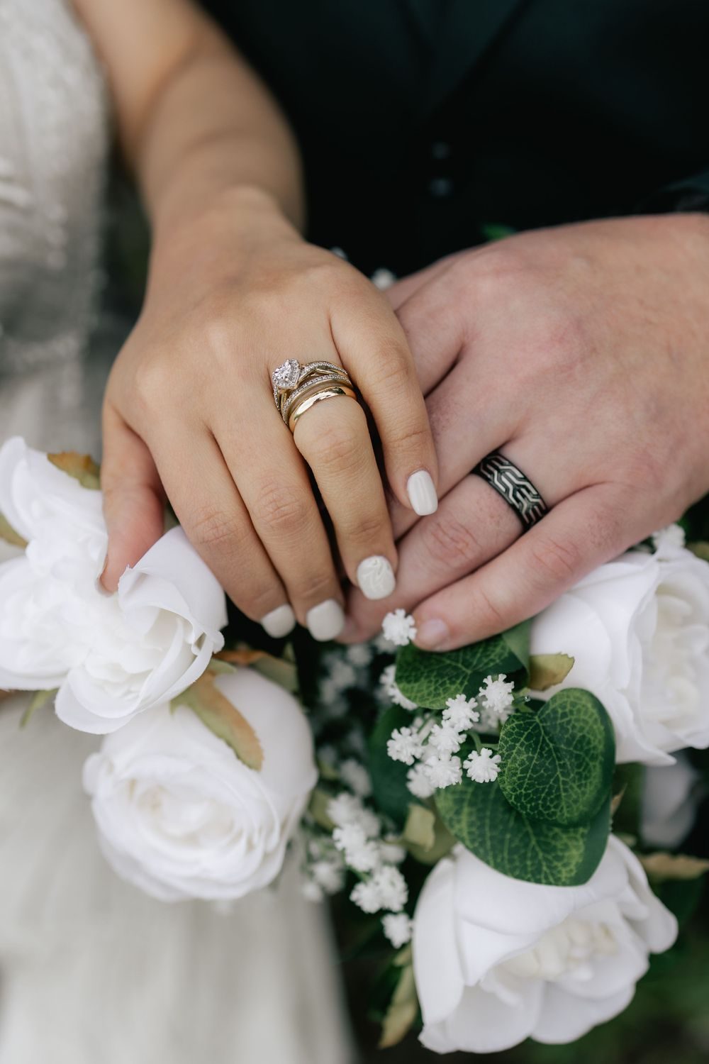 Close-up of the couple's hands and wedding rings resting on white roses.