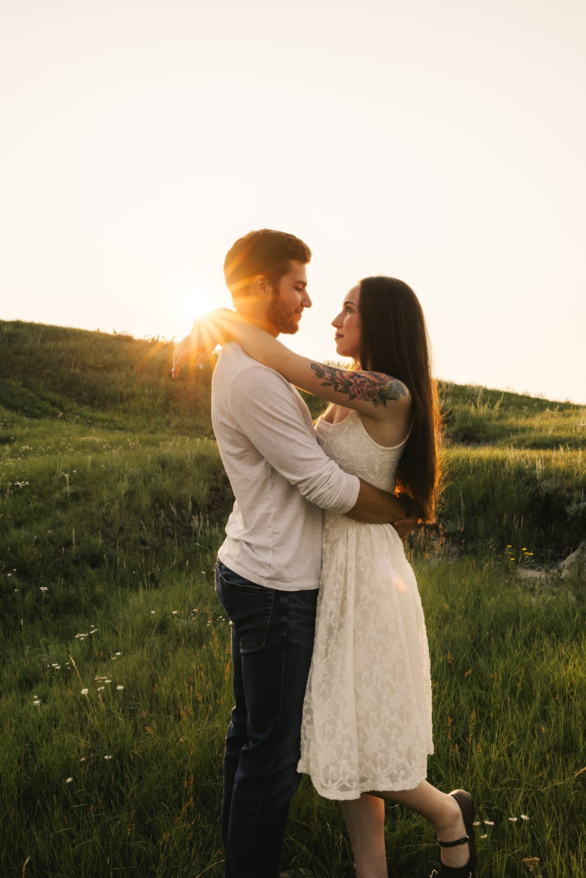 A couple embraces on a grassy hill as the sun sets behind them.