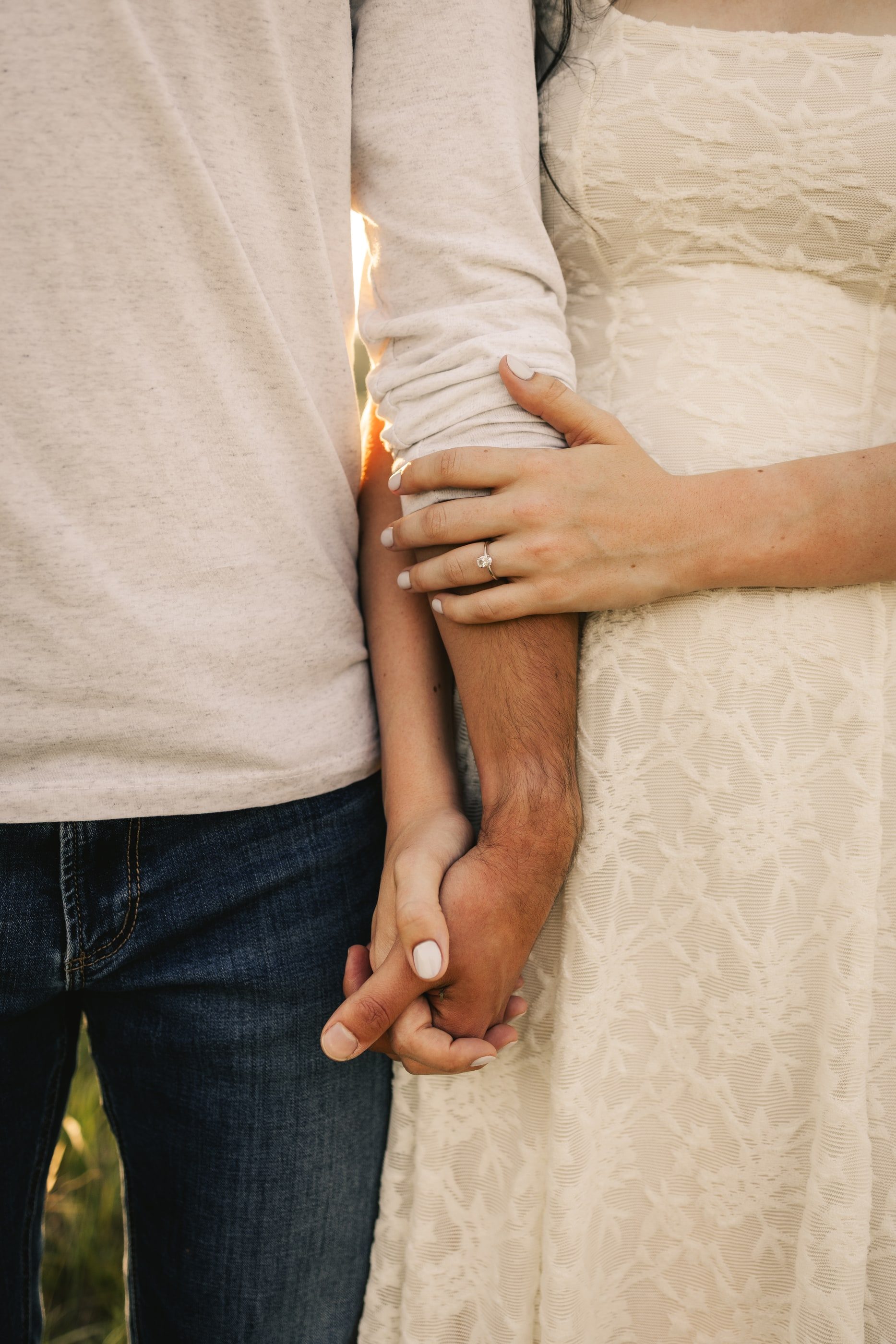 Close-up of a couple holding hands, her engagement ring resting on his arm.