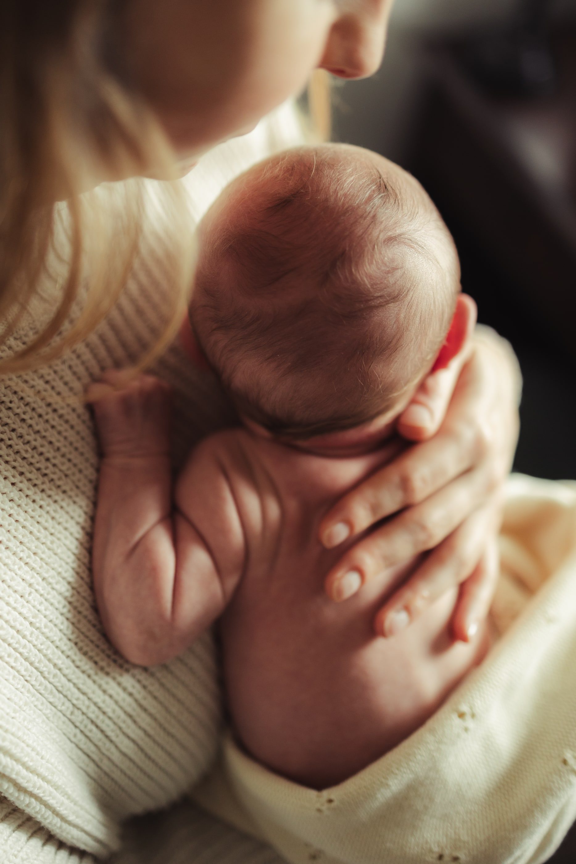 Close-up of a newborn curled against a parent's shoulder, a hand resting on the baby's back.